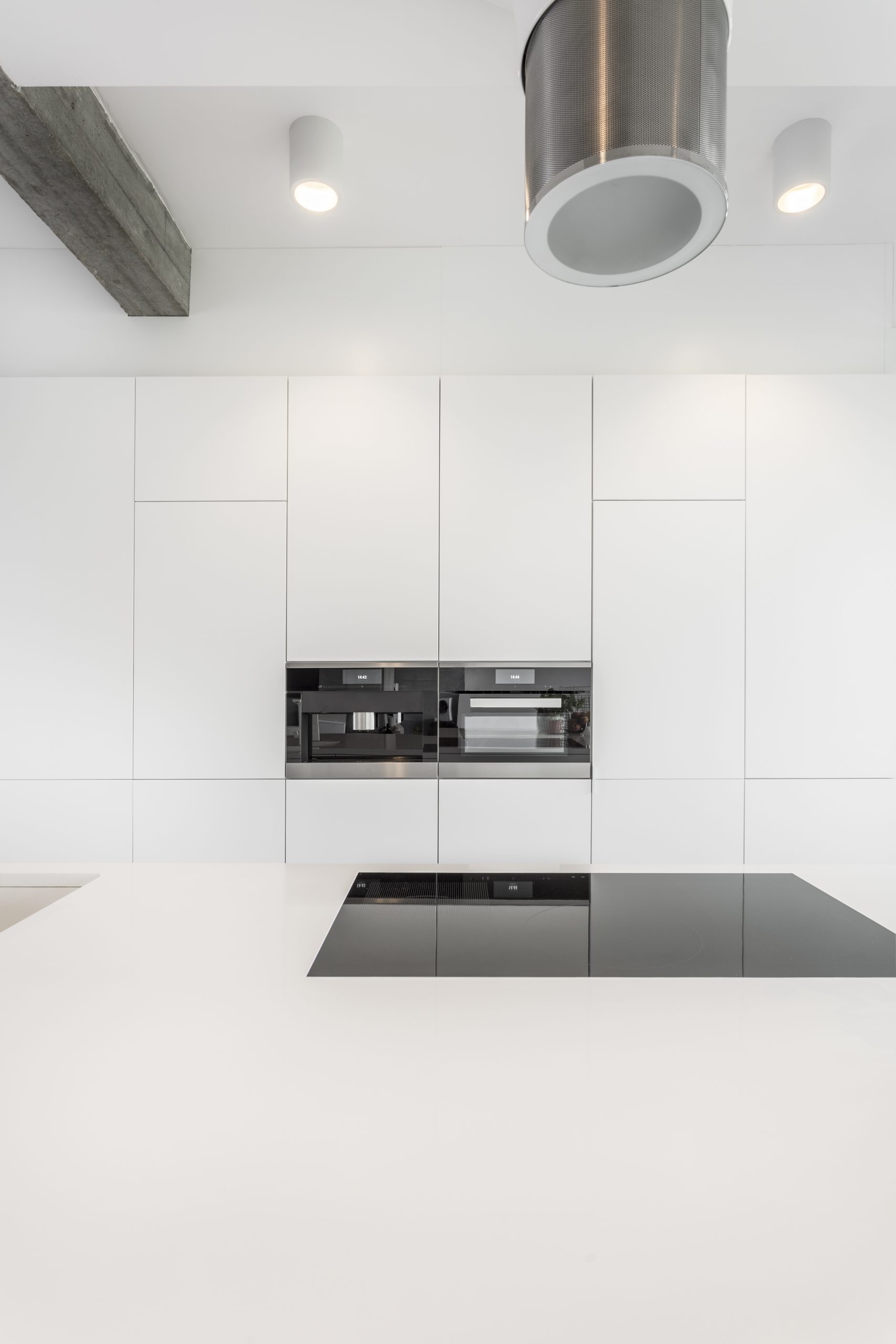 Black oven and microwave in white spacious kitchen with designed hood above glossy induction hob